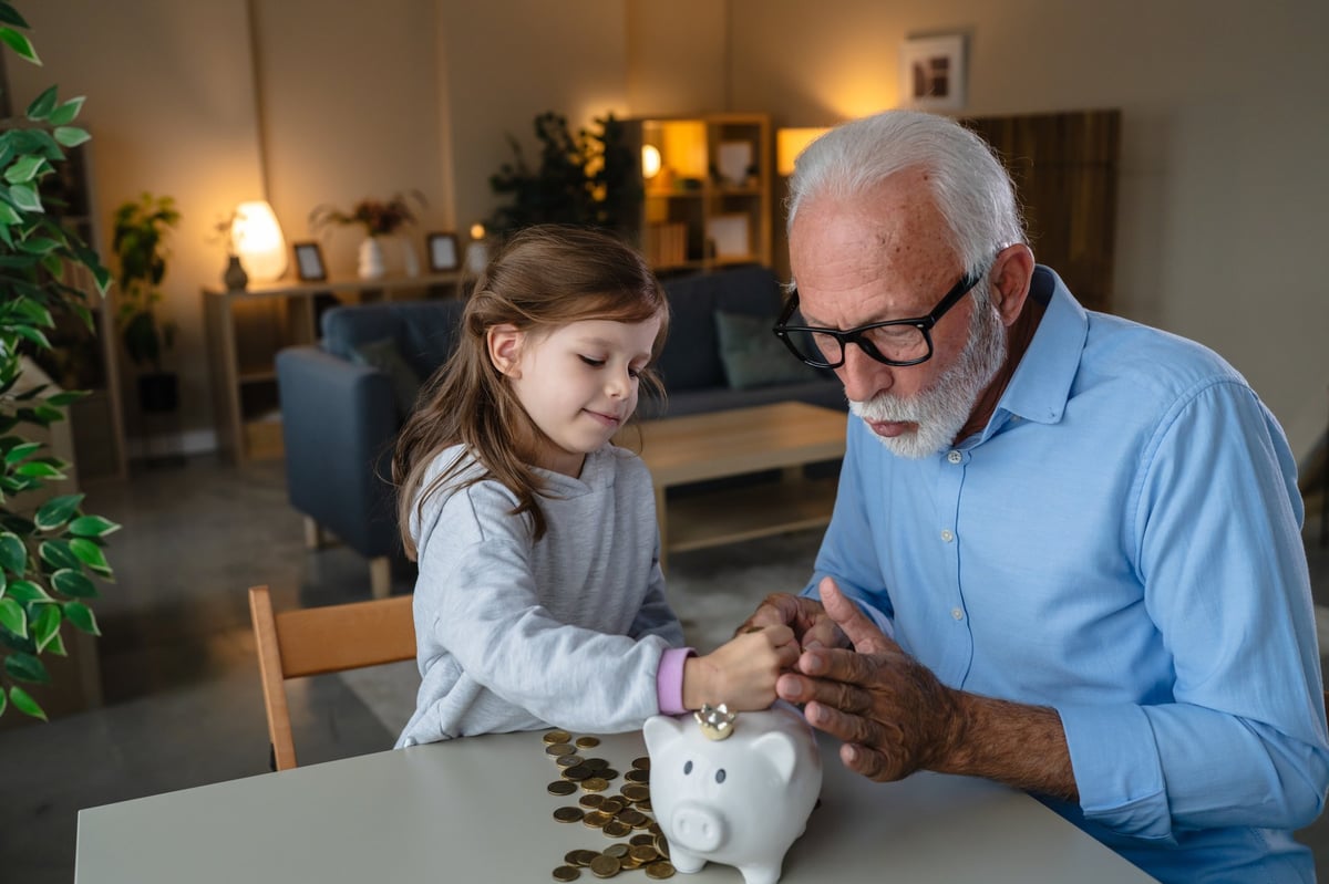 Grandfather teaching his granddaughter about financial literacy and saving money together, creating a warm multi-generational bond